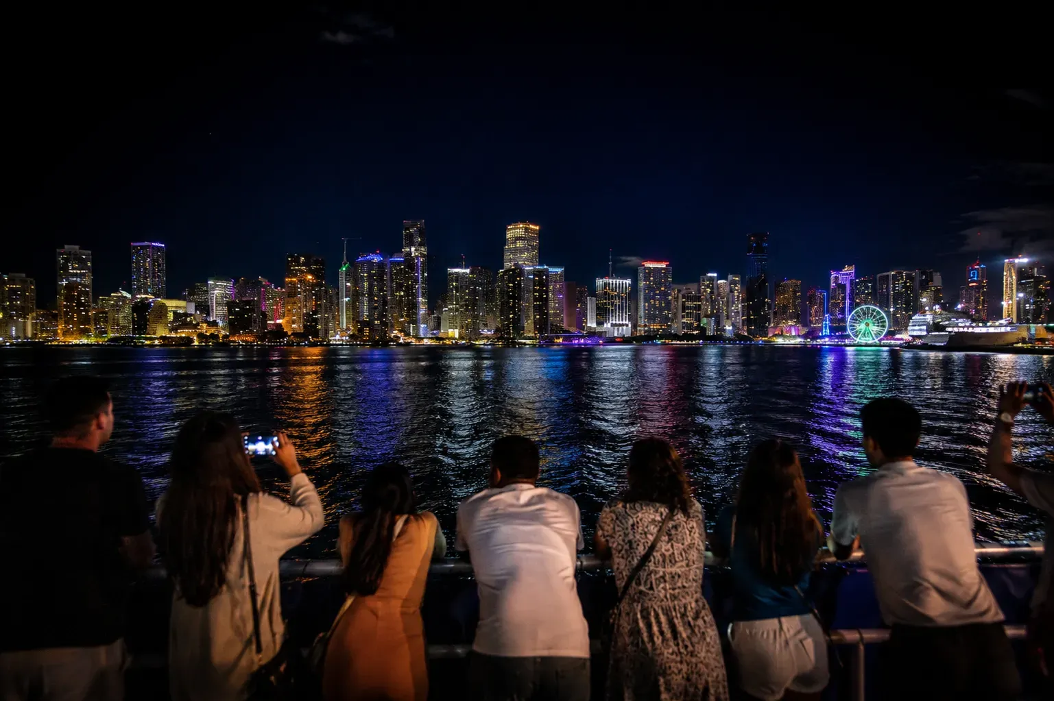 Miami Night Cruise passengers viewing the illuminated Miami skyline from Biscayne Bay.