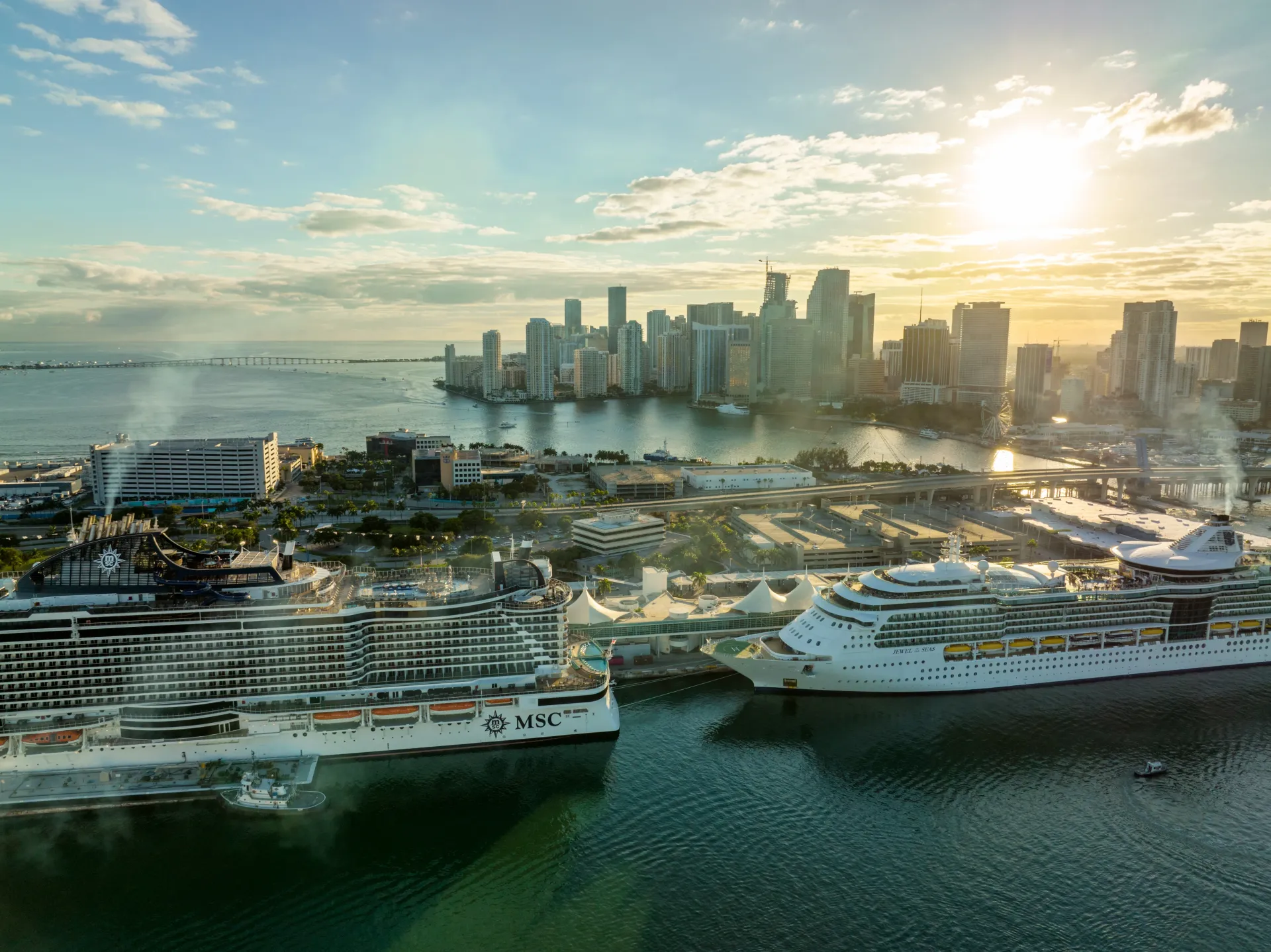 Multiple cruise ships docked at the Port of Miami with the downtown Miami skyline and Biscayne Bay at sunrise.