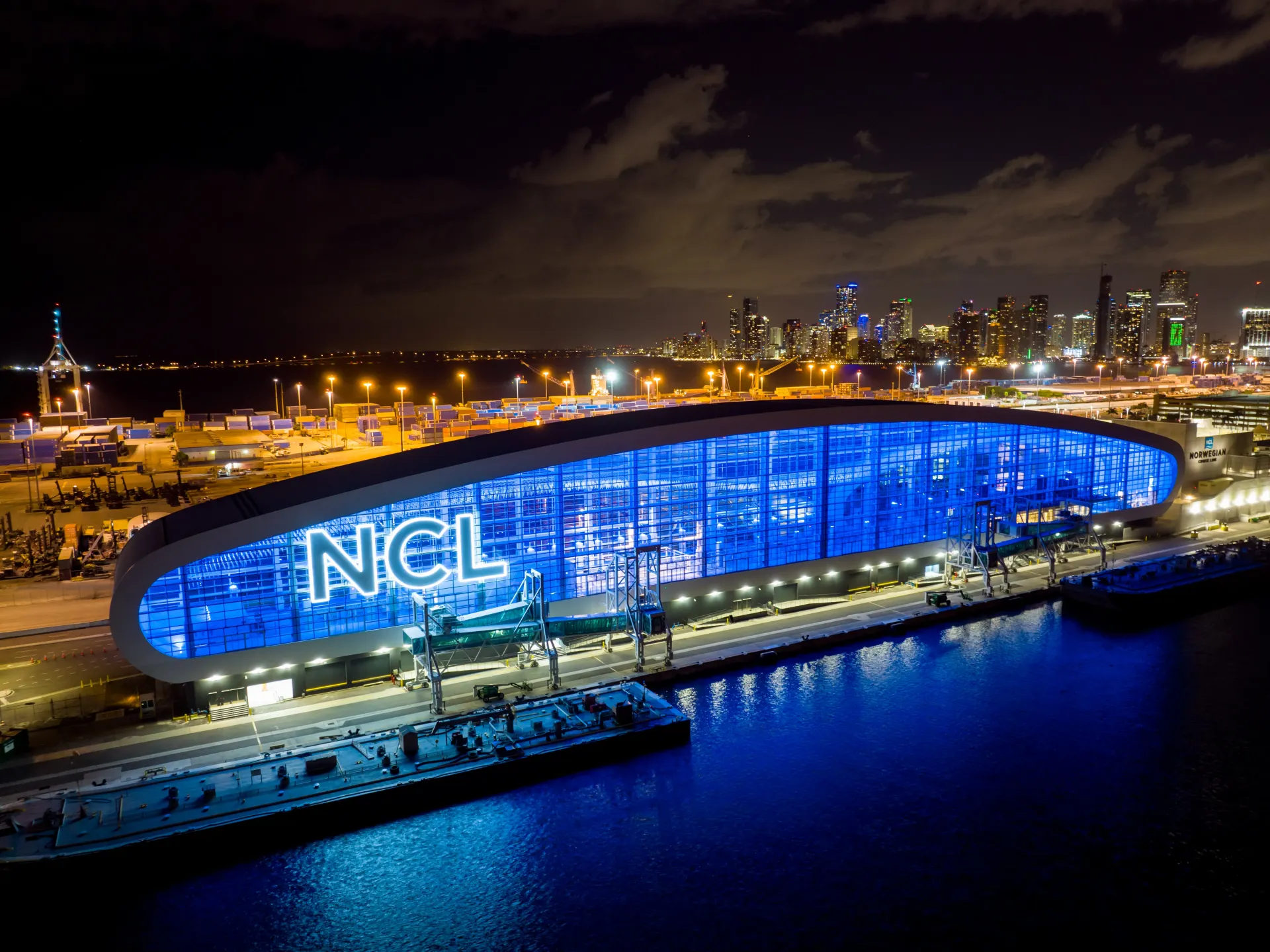 Port of Miami cruise terminal at night with illuminated terminal building and downtown Miami skyline in the background.