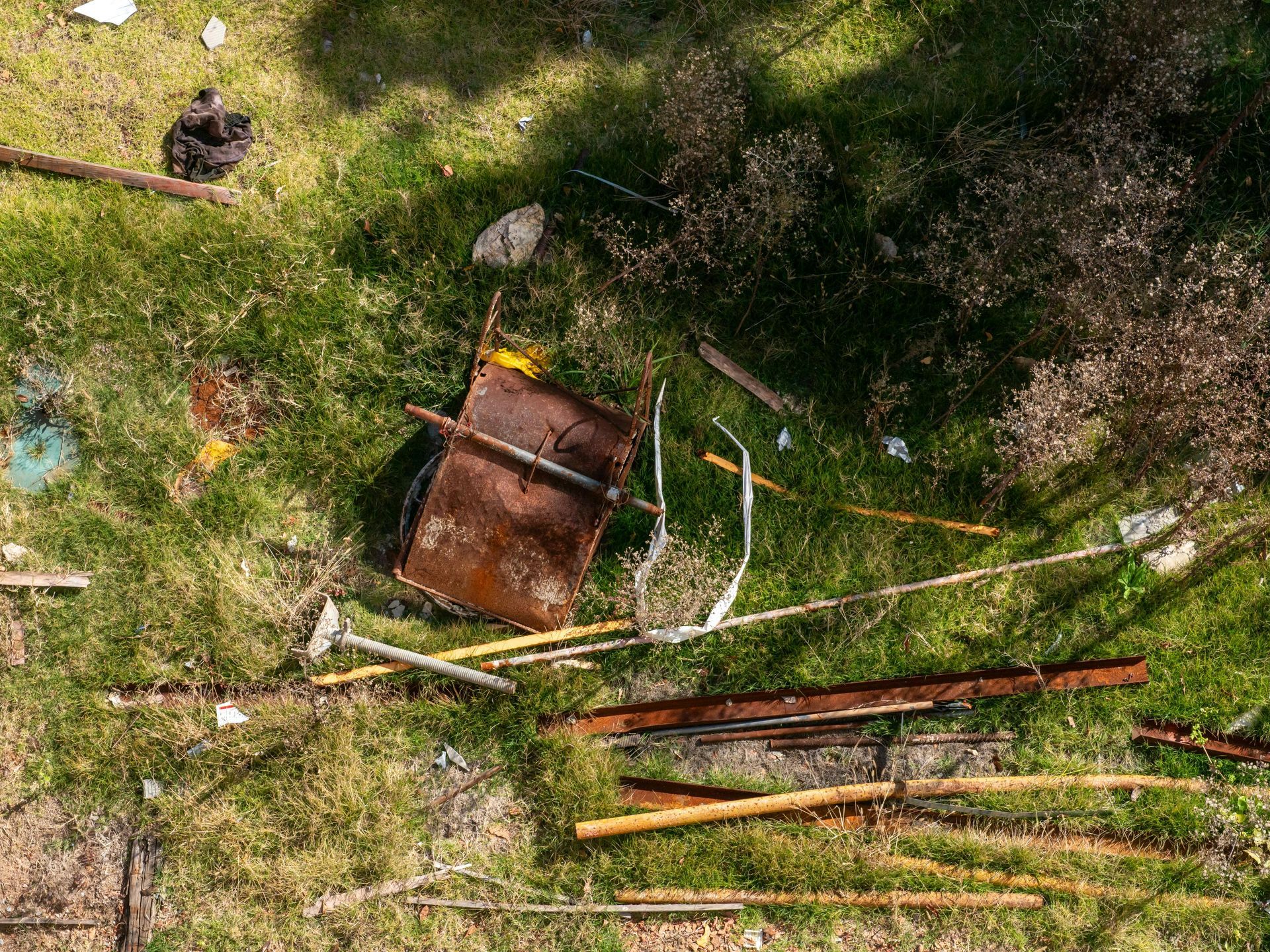An overhead view of discarded scrap metal, rusted panels, and wooden poles scattered across a patch of grass.