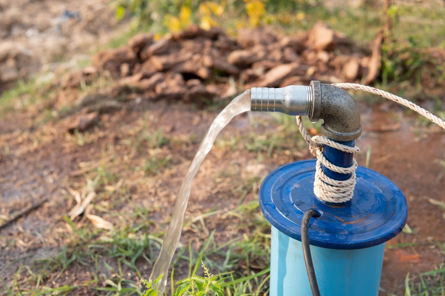 Water flowing from a hose attached to a blue barrel outdoors on the ground.