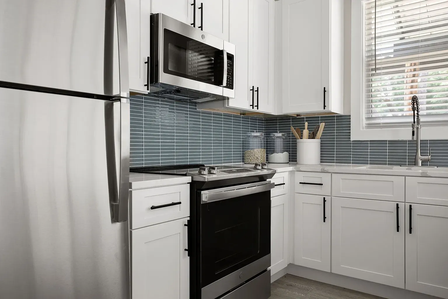 Modern white kitchen with stainless steel appliances, black stove, and striped backsplash by a window