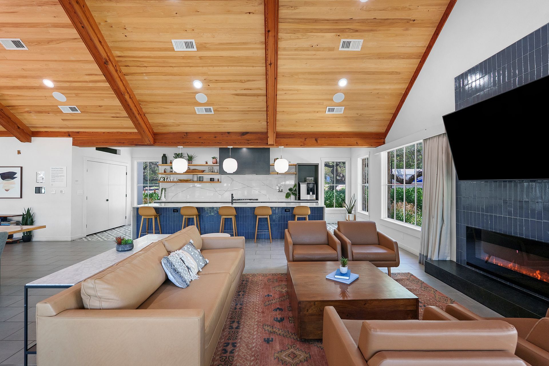 Modern living room with beige sofas, fireplace, and open kitchen under a wood-paneled ceiling