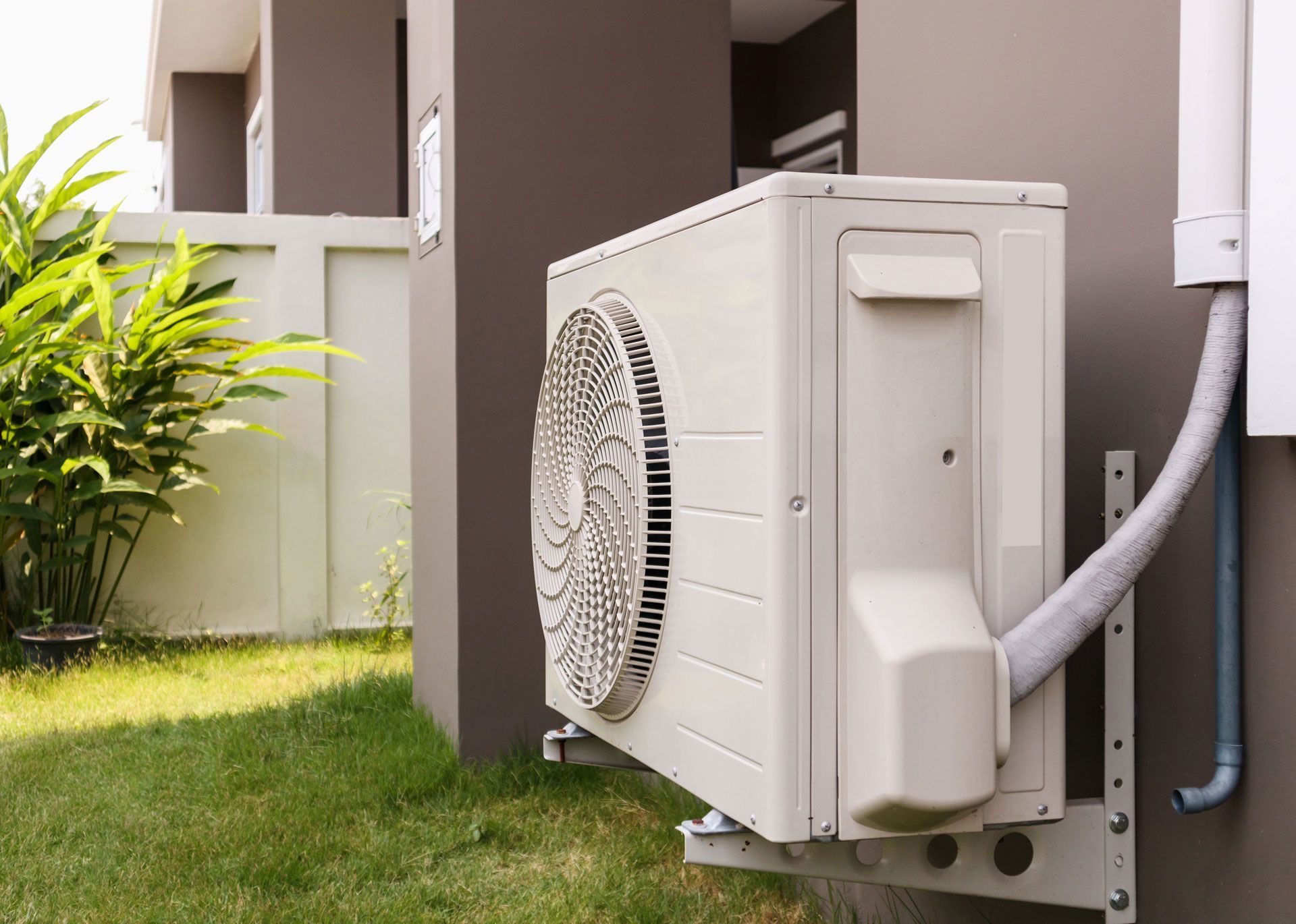 Outdoor air conditioner unit beside a building, with a hose connected and grass nearby