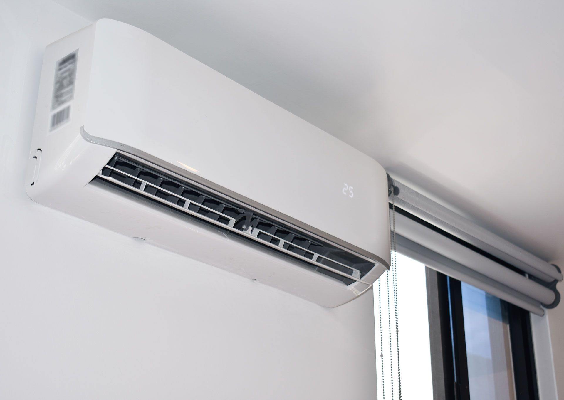 White wall-mounted air conditioner above a window with blinds in a bright room