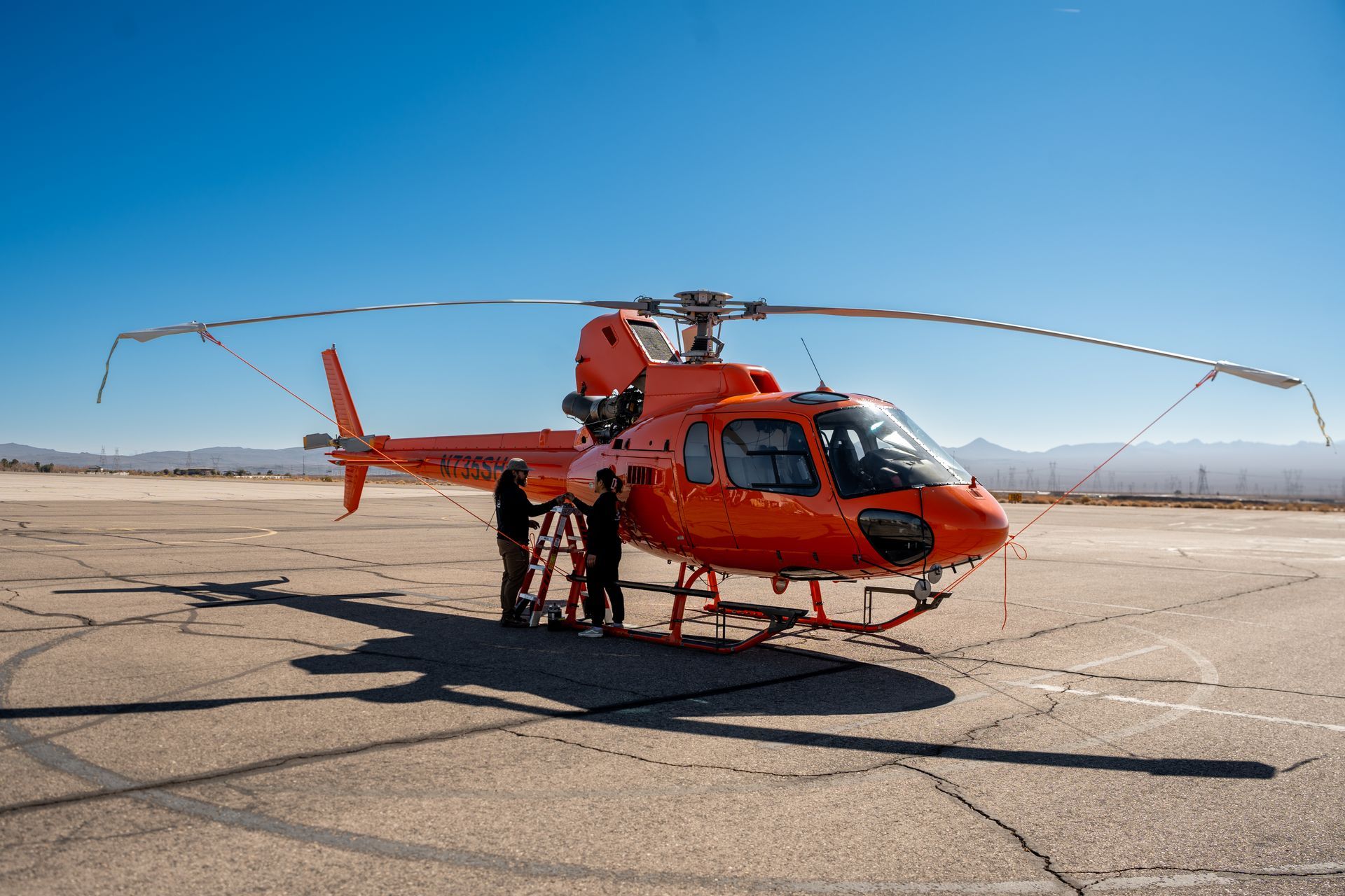An orange helicopter is parked on a runway.