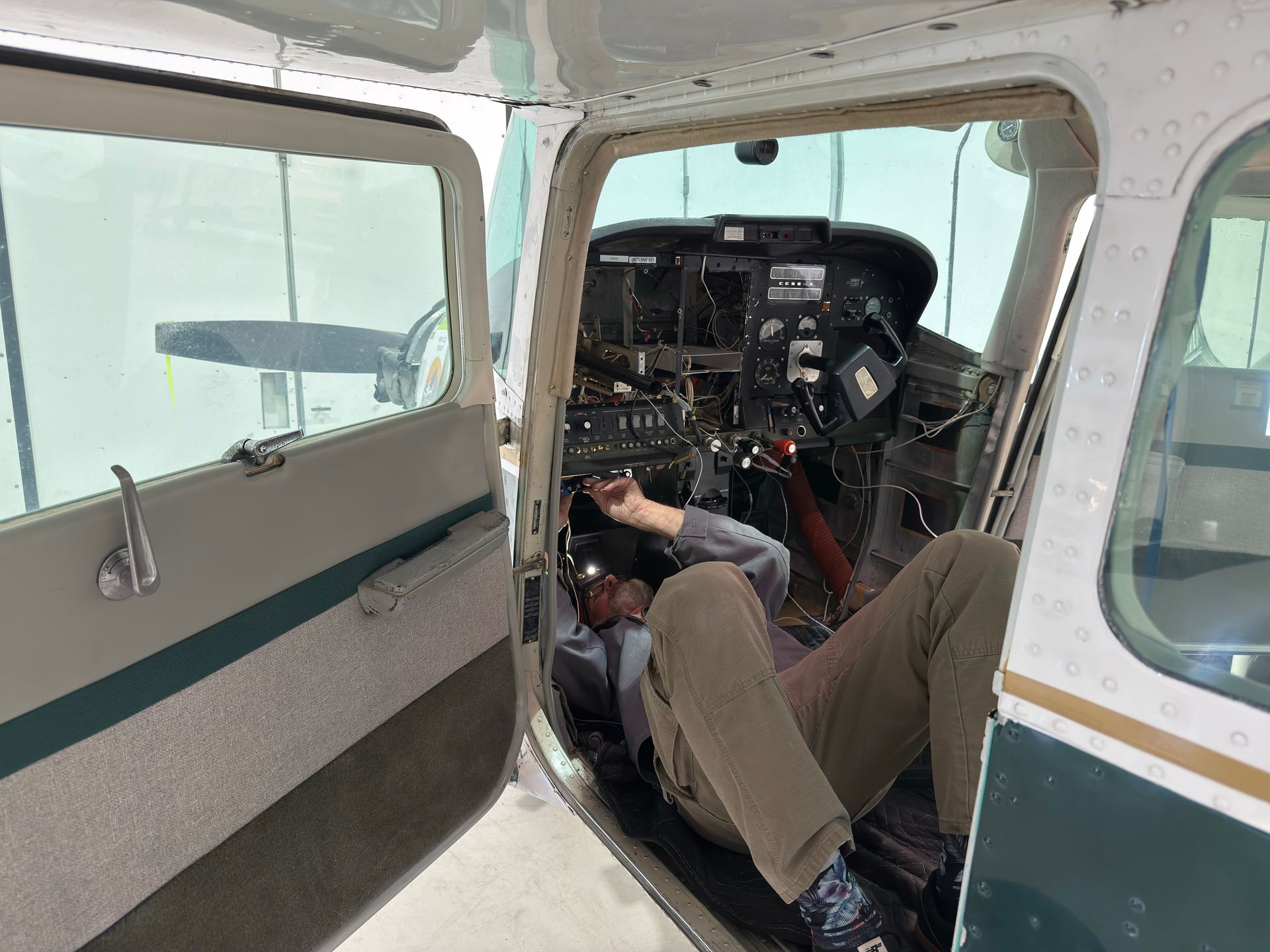 Aircraft technician working on avionics wiring beneath an instrument panel during an avionics upgrad