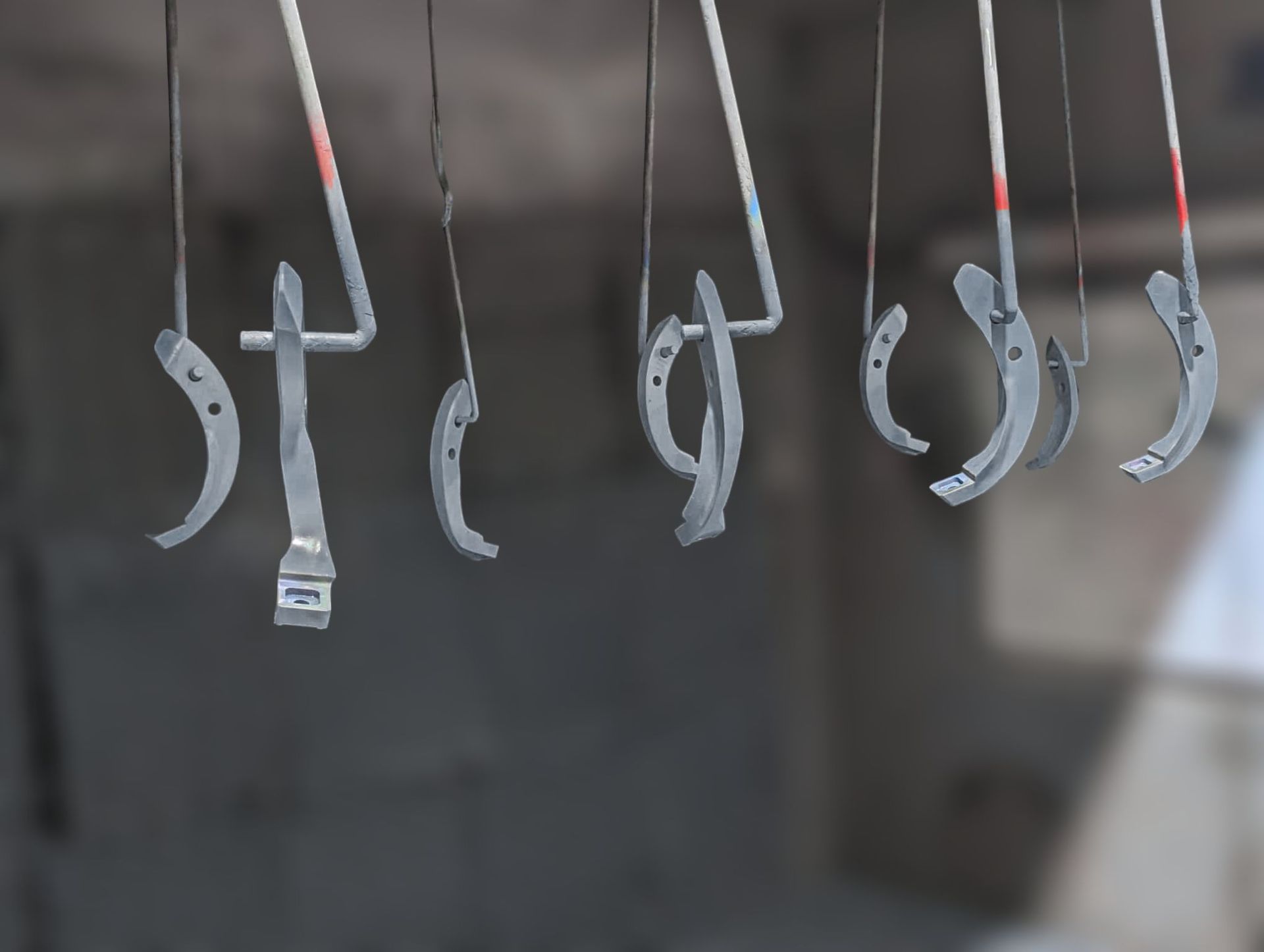 Several metal hooks hanging from wires against a blurred gray background