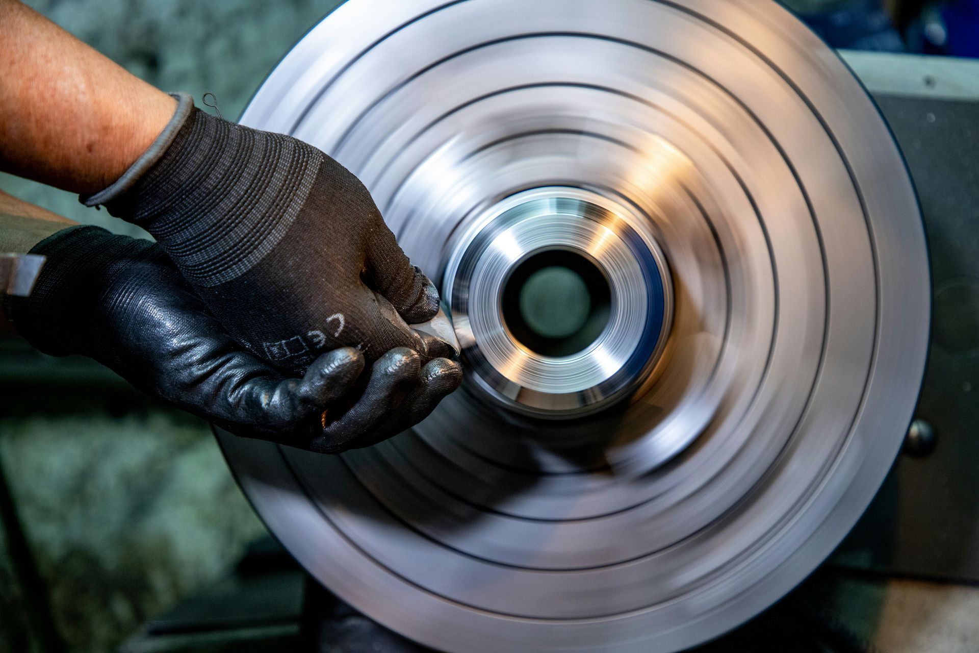 Gloved hands polishing a spinning metal wheel on a lathe or grinder
