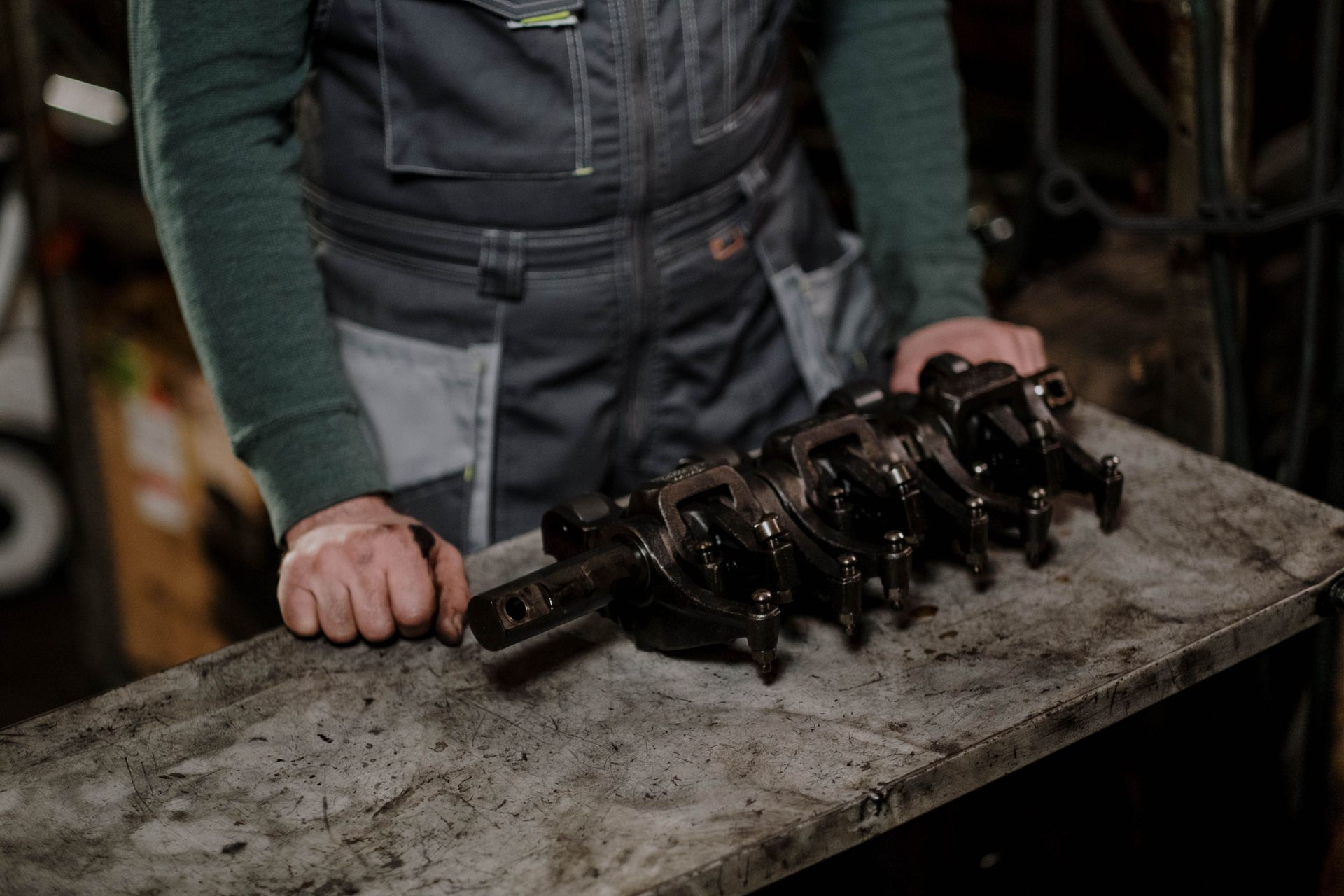 Person holding a rusty metal crankshaft on a workbench in a workshop