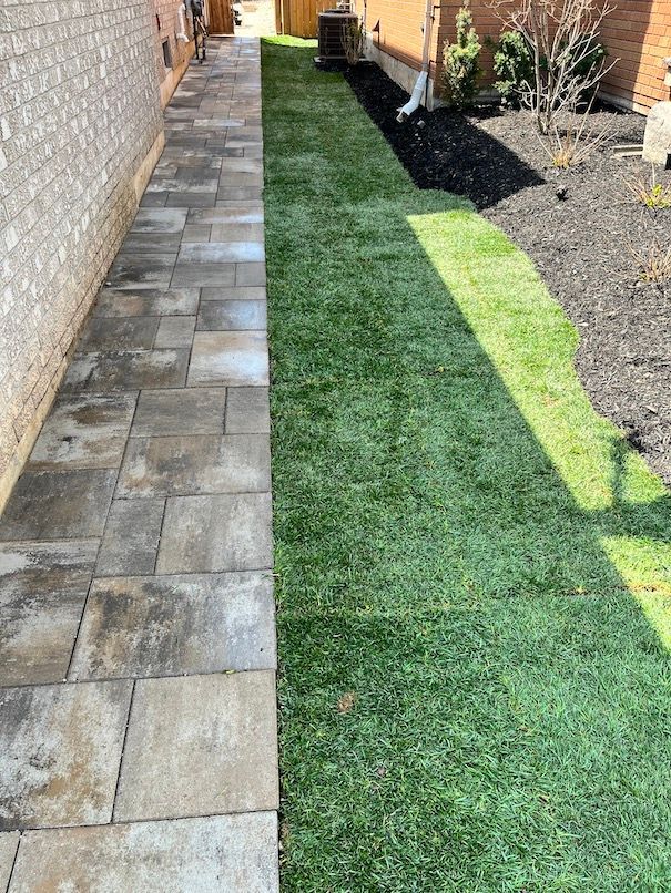 A sidewalk leading to a lush green lawn next to a brick building.