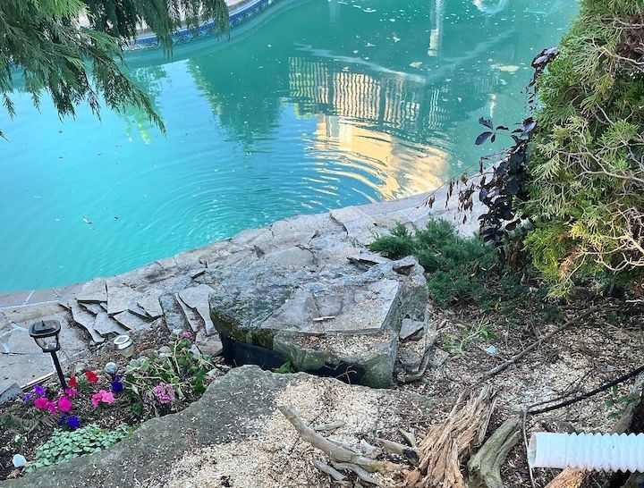 A large rock is sitting next to a swimming pool.