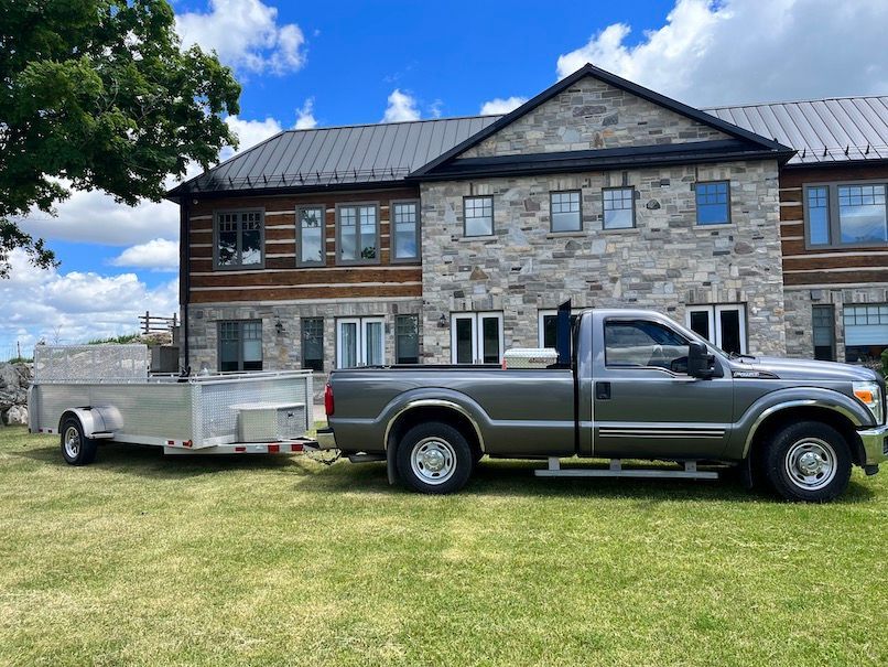 A truck with a trailer attached to it is parked in front of a large house.