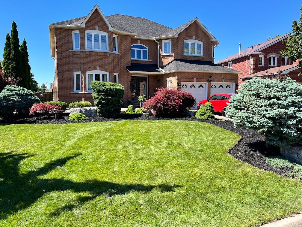 A large brick house with a lush green lawn and a red car parked in front of it.