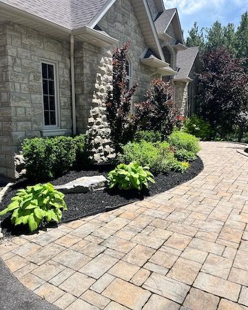 A brick walkway leading to a large brick house surrounded by plants and bushes.