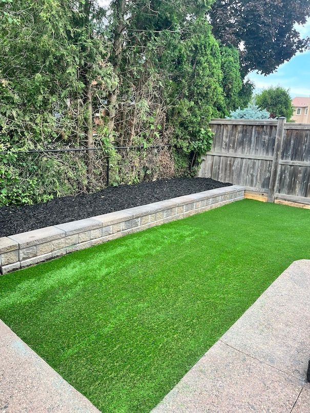 A backyard with a brick wall , a fence , and a lush green lawn.
