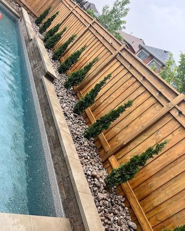 A wooden fence surrounds a swimming pool with trees and rocks.