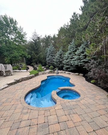 A large swimming pool with a hot tub in the backyard surrounded by trees.