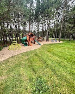 A playground in the middle of a lush green field surrounded by trees.