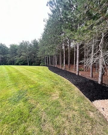 A lush green field surrounded by trees and black mulch.