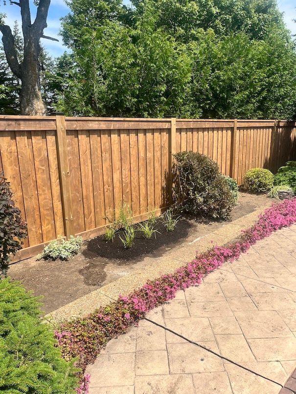 A wooden fence is surrounded by flowers and trees in a backyard.