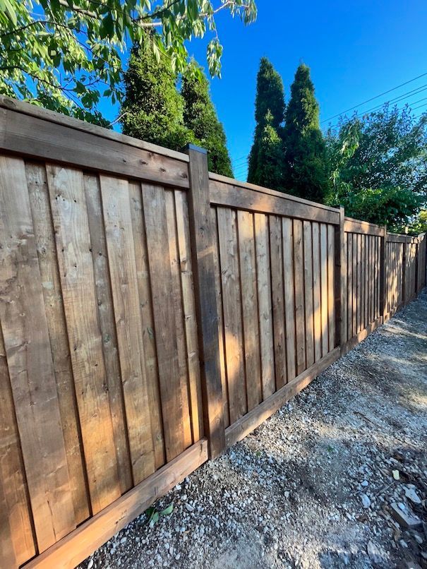 A wooden fence along a dirt road with trees in the background.