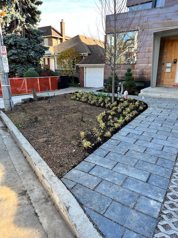 A brick walkway leading to a house with a garden in front of it.