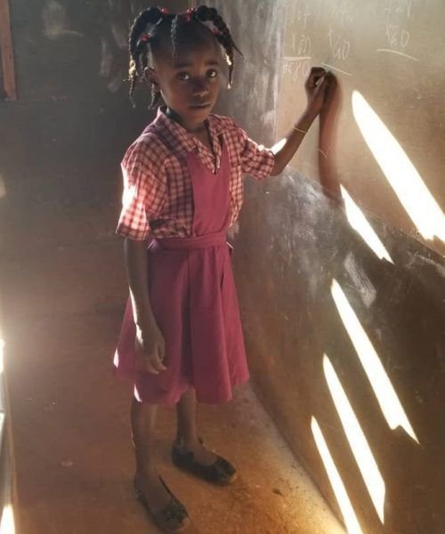 A little girl in a pink dress is writing on a blackboard