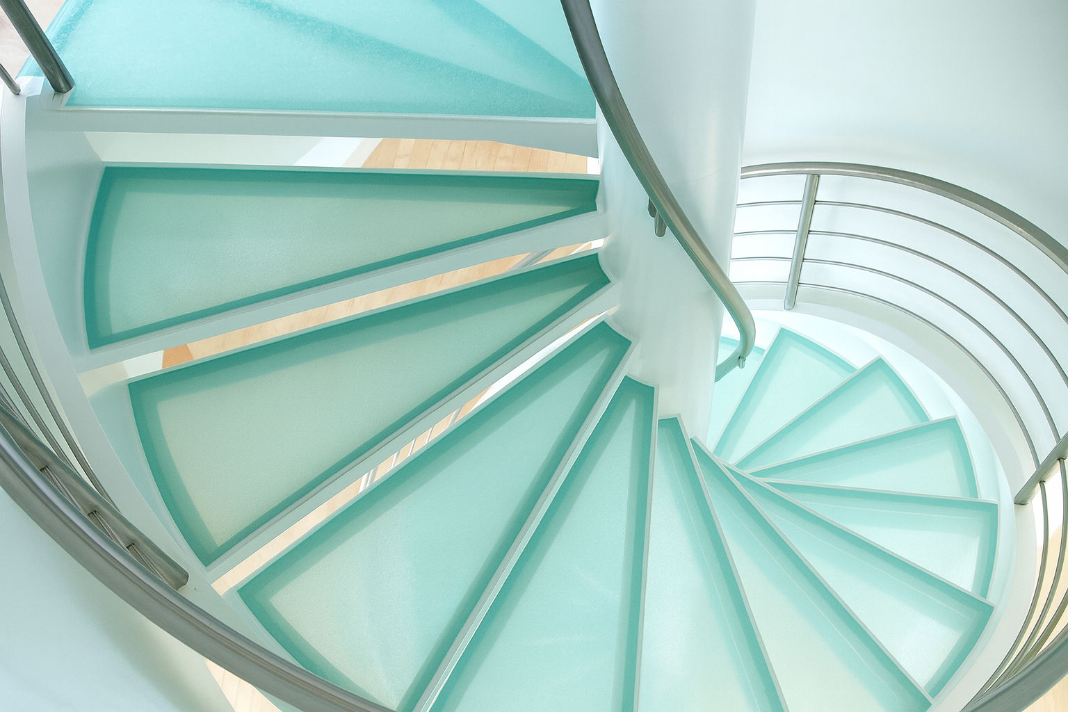 Spiral staircase with teal glass steps and a silver railing.