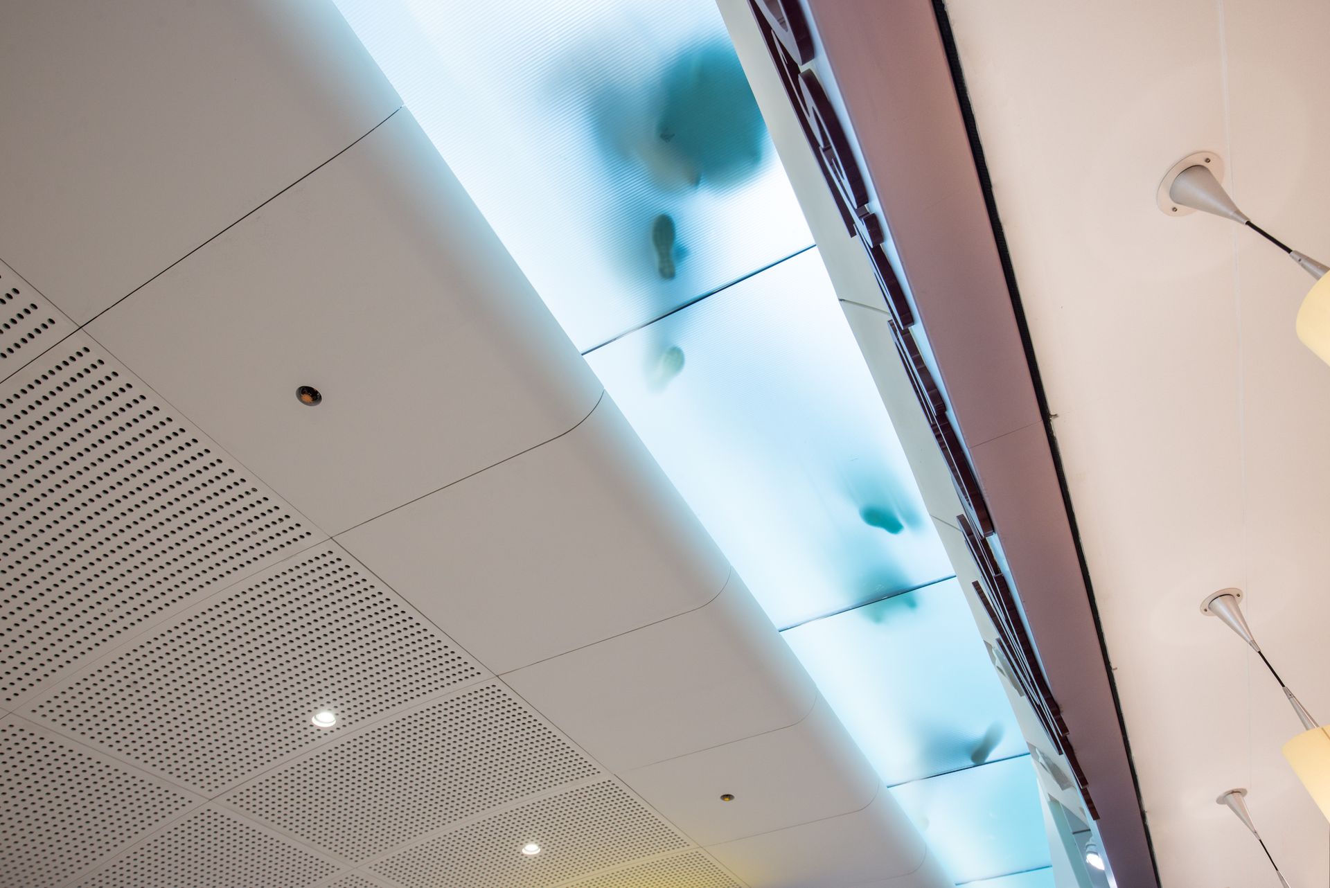 People walking on a glass ceiling panel with blue lighting, viewed from below.