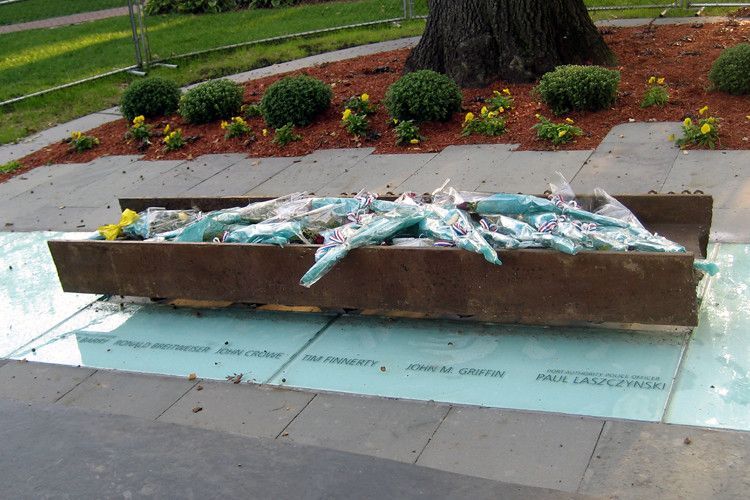 Wooden trough filled with debris, resting on blue foam insulation on a sidewalk, with landscaping in background.