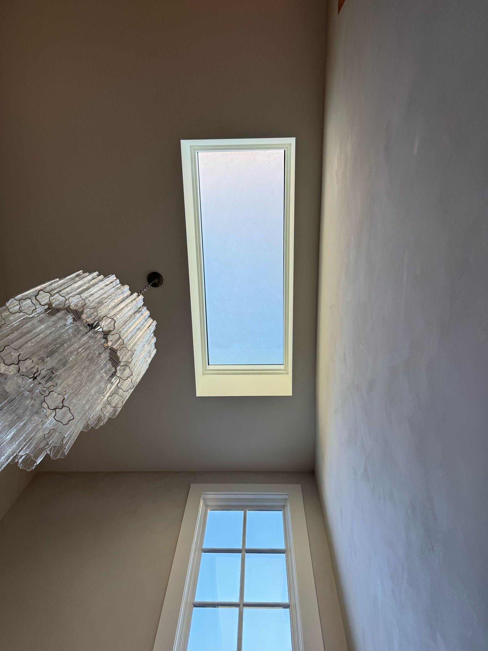 walkable skylight and window in a room, overhead view, chandelier hangs on the left, bright sky visible.