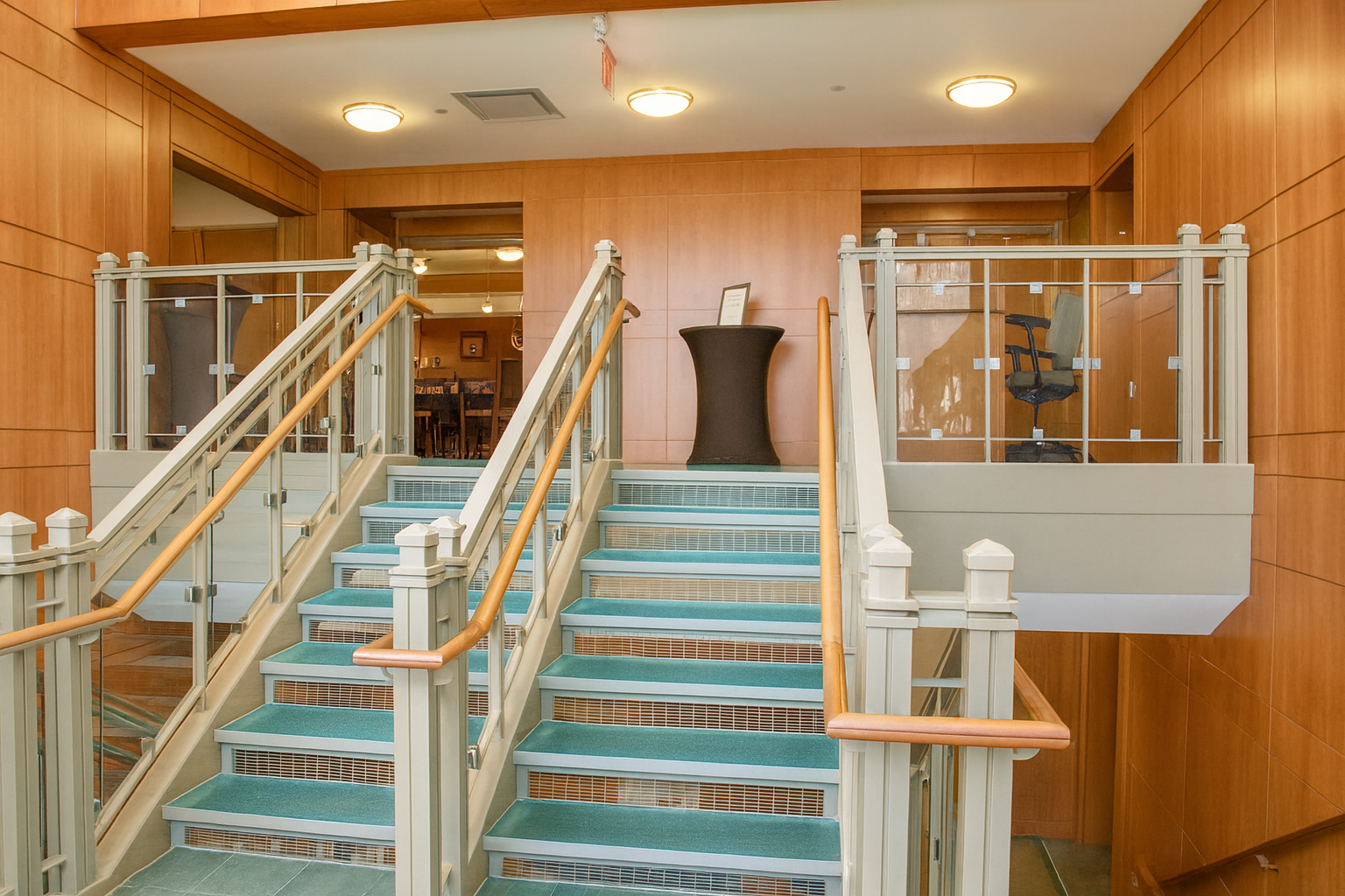 Wooden-paneled entry with teal carpeted stairs, glass railings, and a small table.