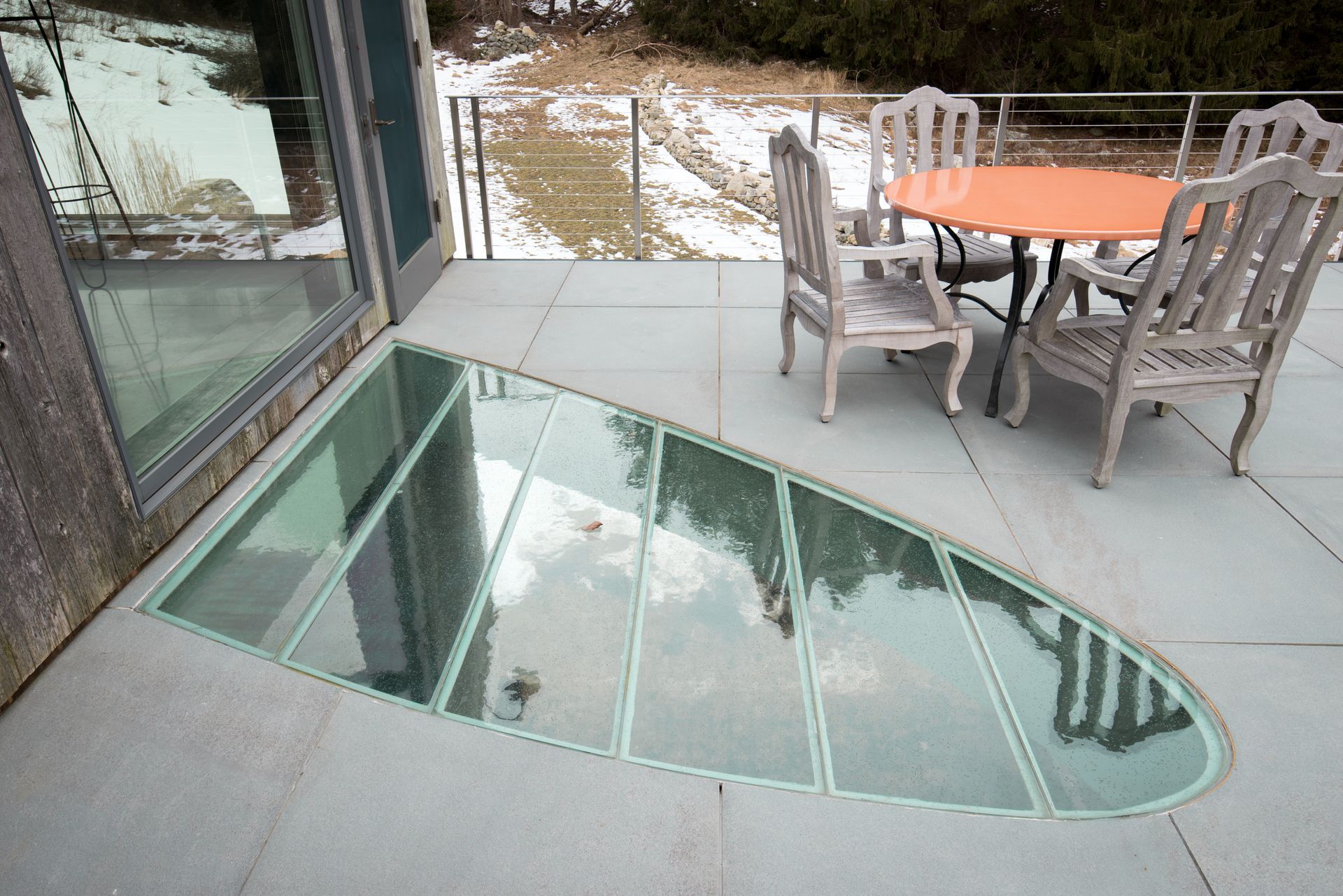 Glass floor section on patio, showing below-level space. Outdoor table/chairs are nearby.