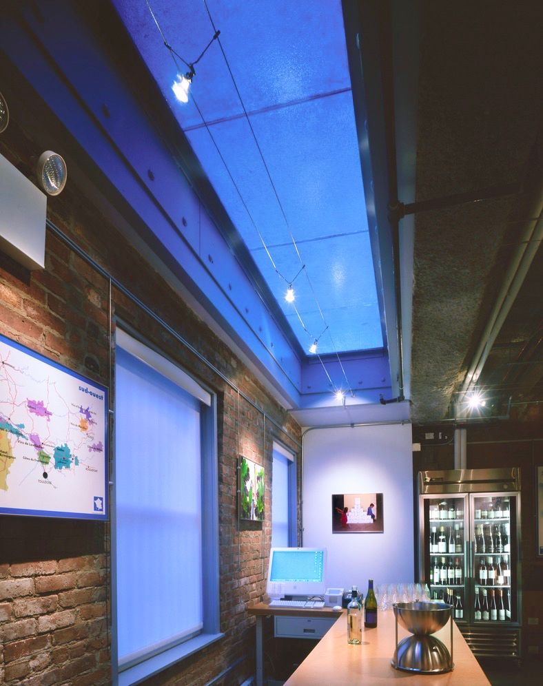 Interior of a restaurant with exposed brick walls, a glass walkable skylight with blue lighting, and a bar.