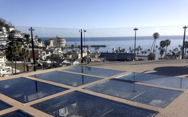 Overlook with glass floor panels, view of harbor town, ocean, and clear sky.