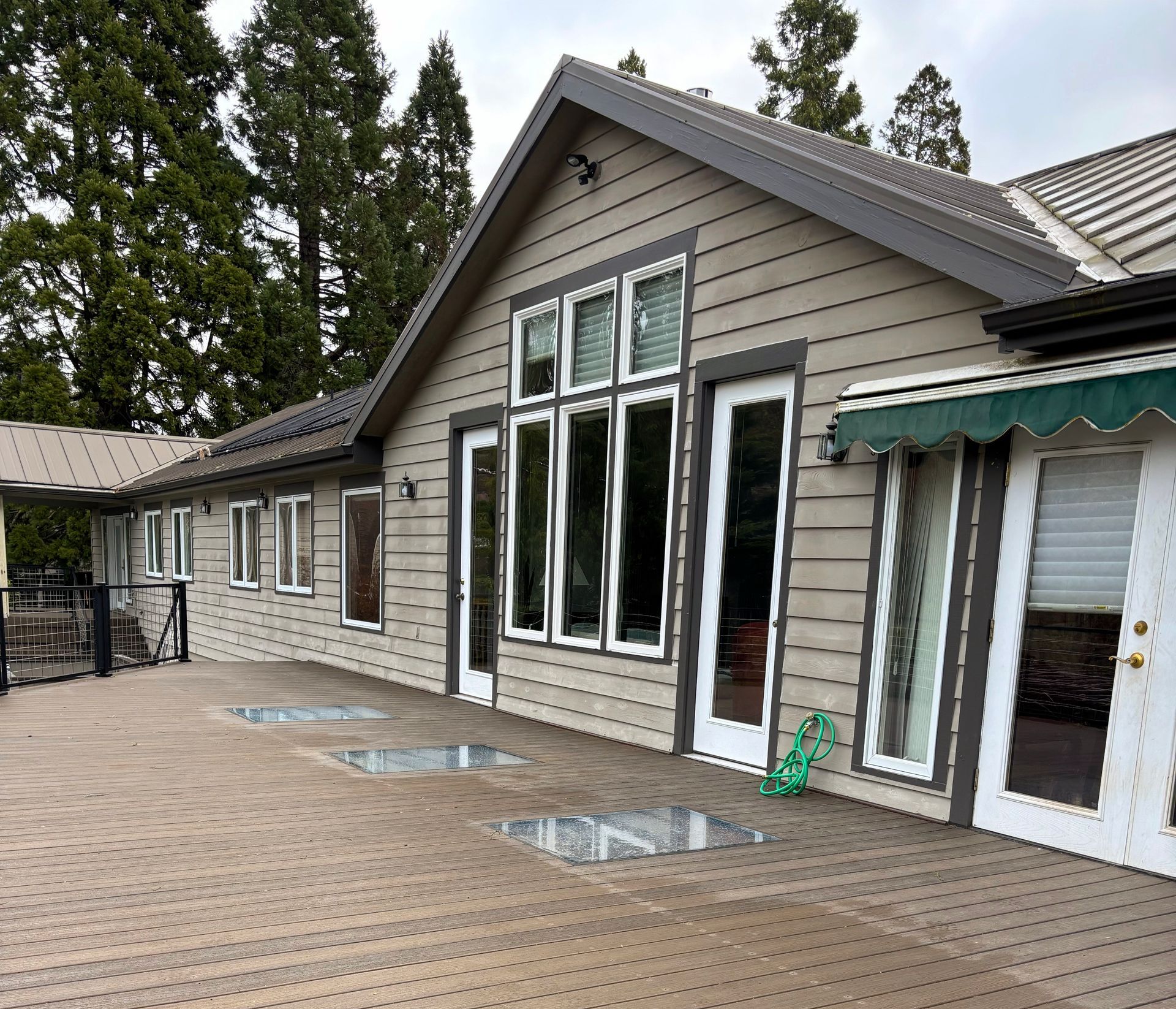 House exterior with a wooden deck, large windows, and a green awning with glass flooring.