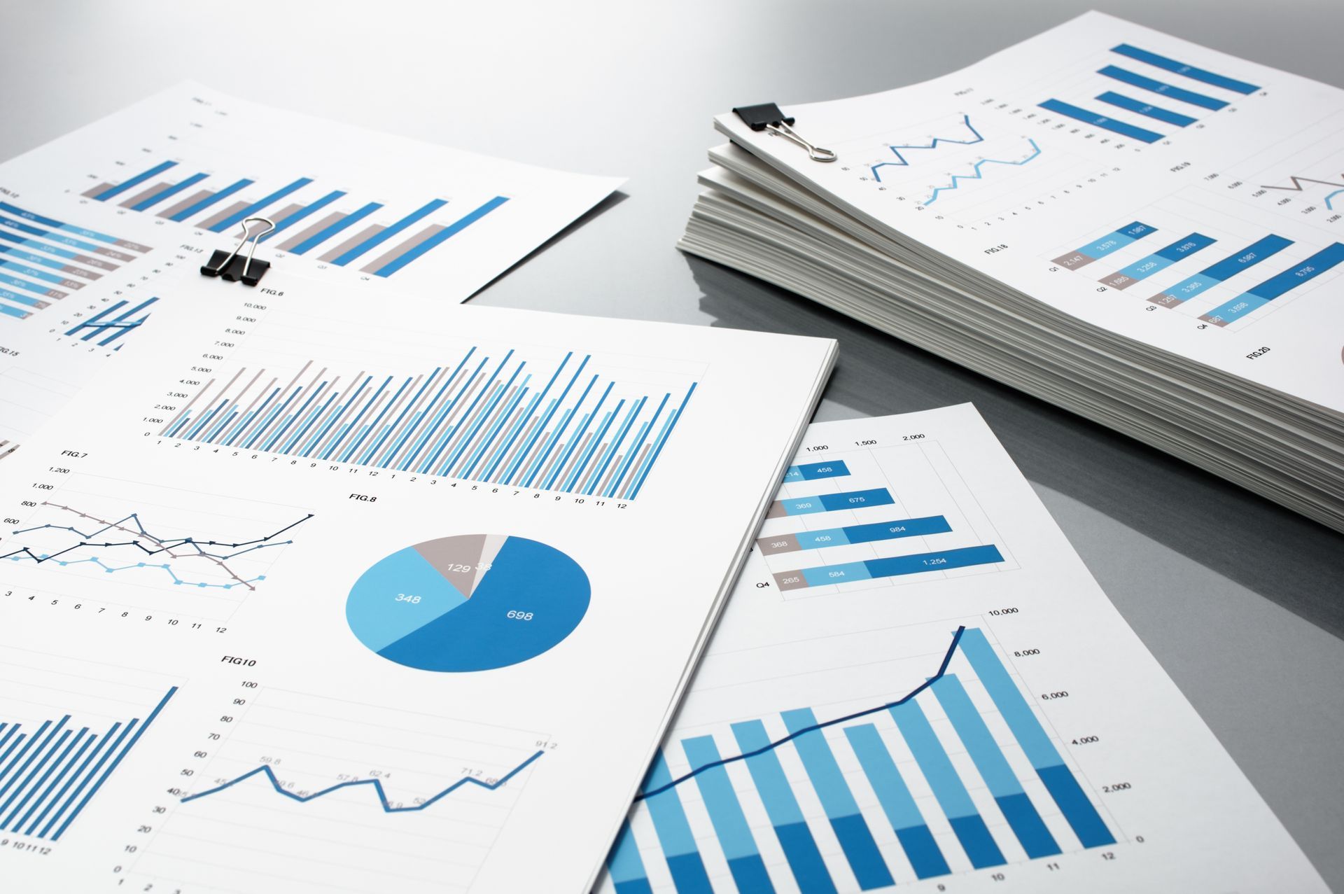 Printed business charts and graphs on white paper, including blue bar and pie charts on a desk. Printed business charts and graphs on white paper, including blue bar and pie charts on a desk.