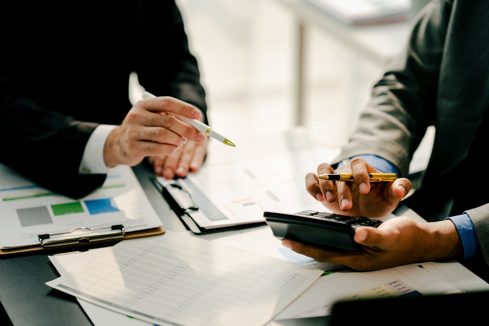 Two people discussing paperwork at a desk, one holding a pen and the other using a phone.