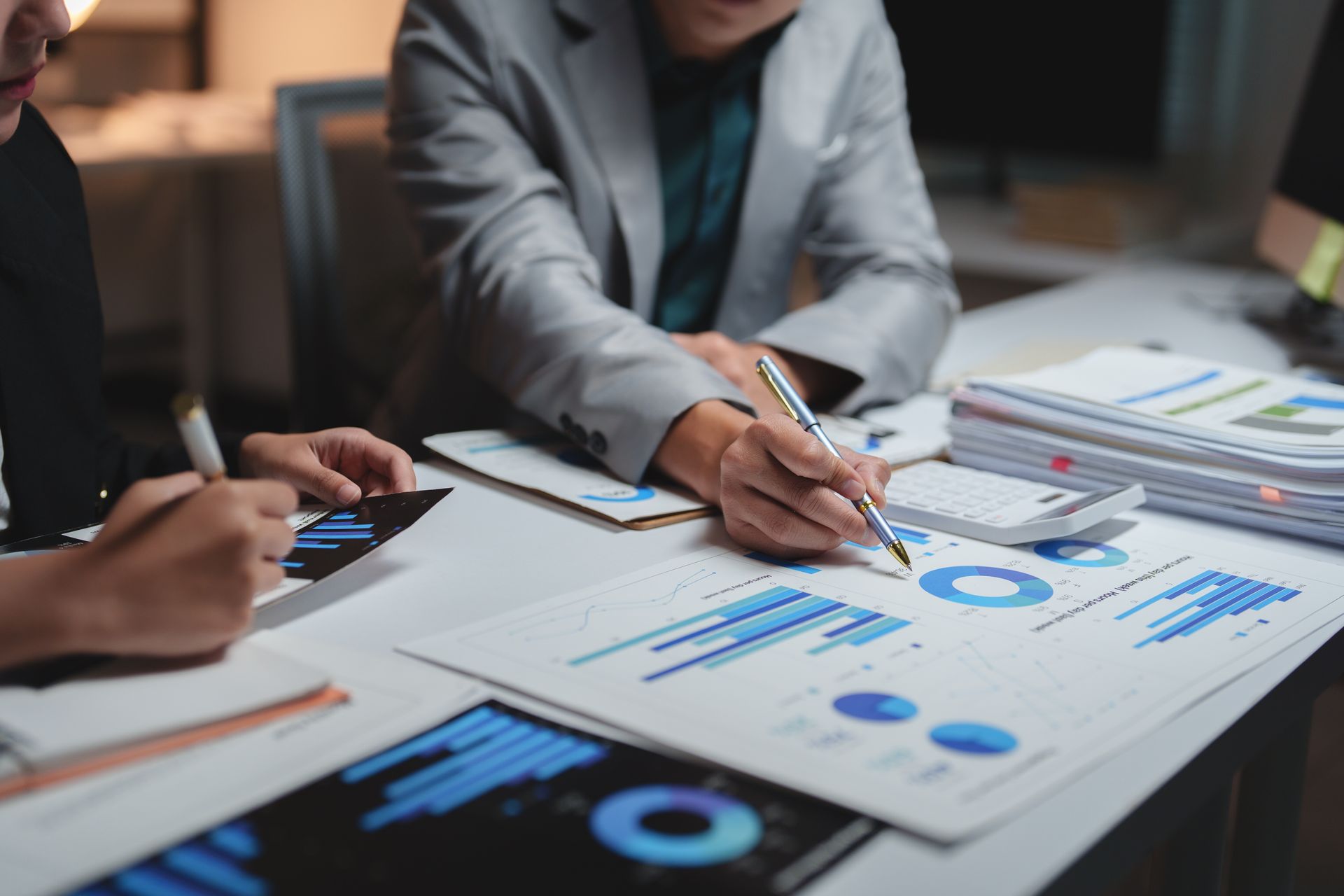People reviewing blue charts and graphs on printed reports at a meeting table People reviewing blue charts and graphs on printed reports at a meeting table