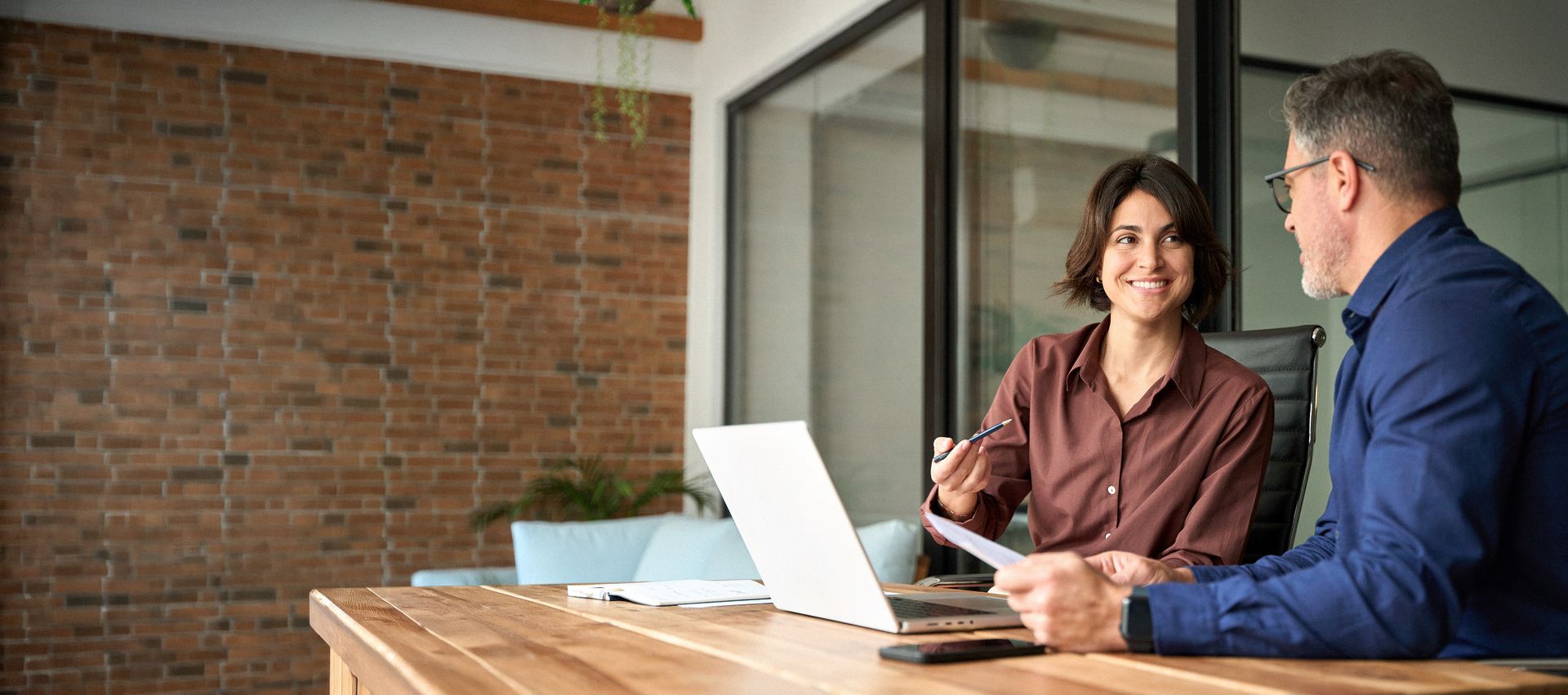 Two people talking at a table with a laptop in a modern office lounge Two people talking at a table with a laptop in a modern office lounge