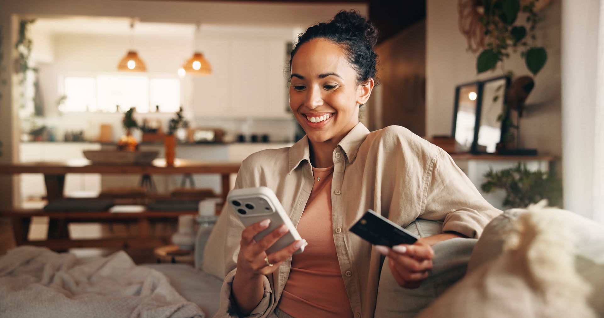 Woman smiling on a couch, holding a phone and credit card in a cozy living room Woman smiling on a couch, holding a phone and credit card in a cozy living room