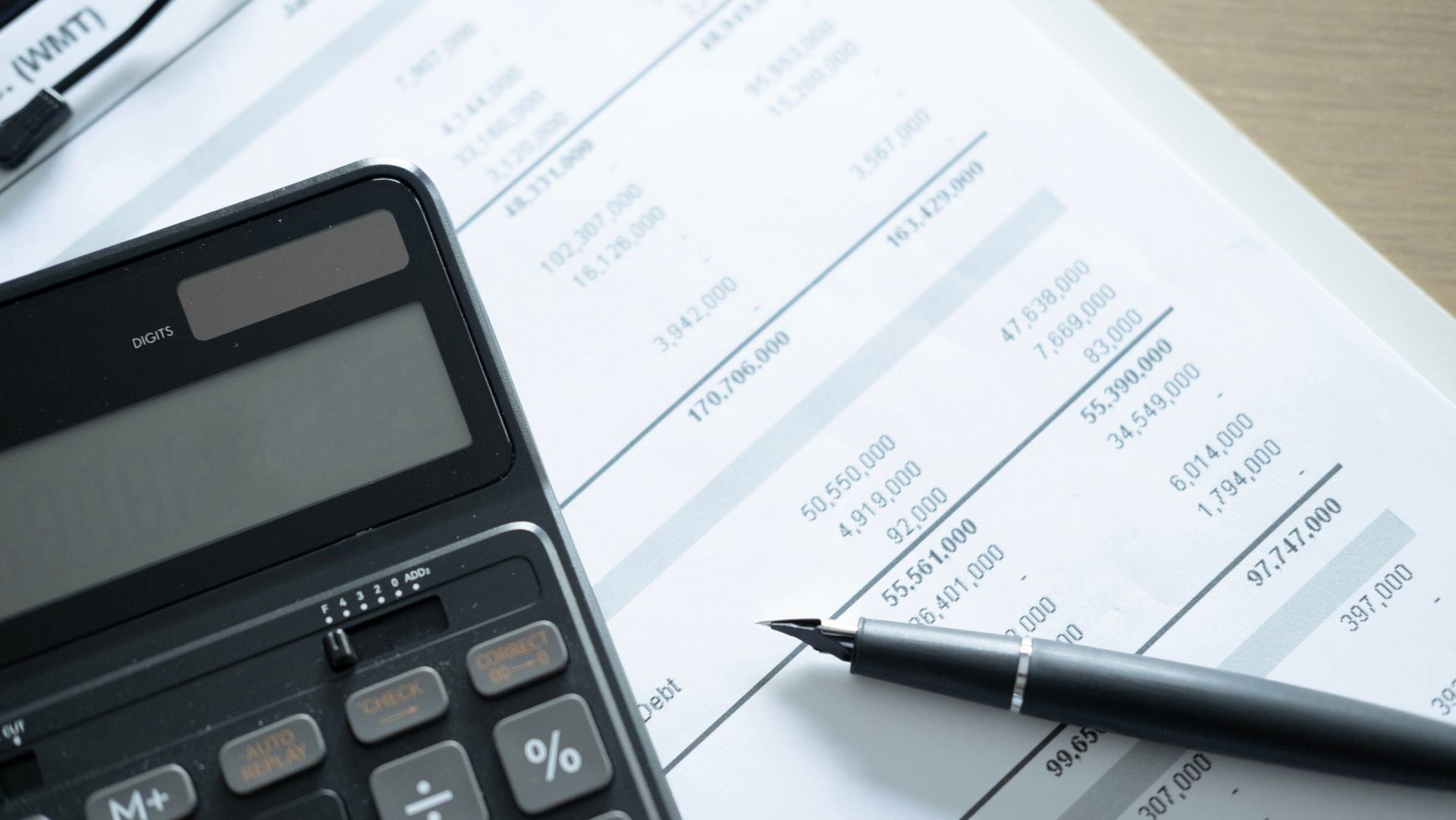 Calculator and pen on financial paperwork with visible columns and totals