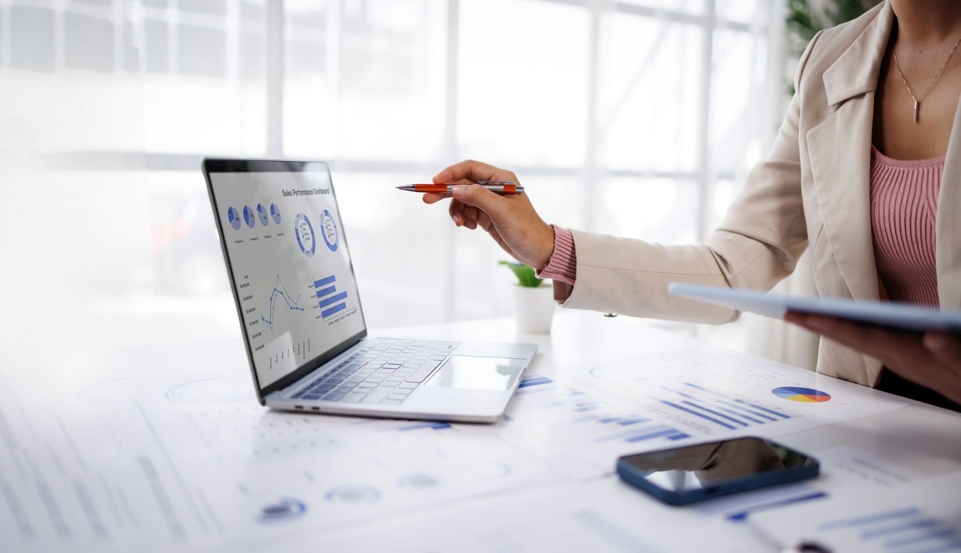 Person pointing at a laptop displaying charts during a business meeting at a bright desk Person pointing at a laptop displaying charts during a business meeting at a bright desk