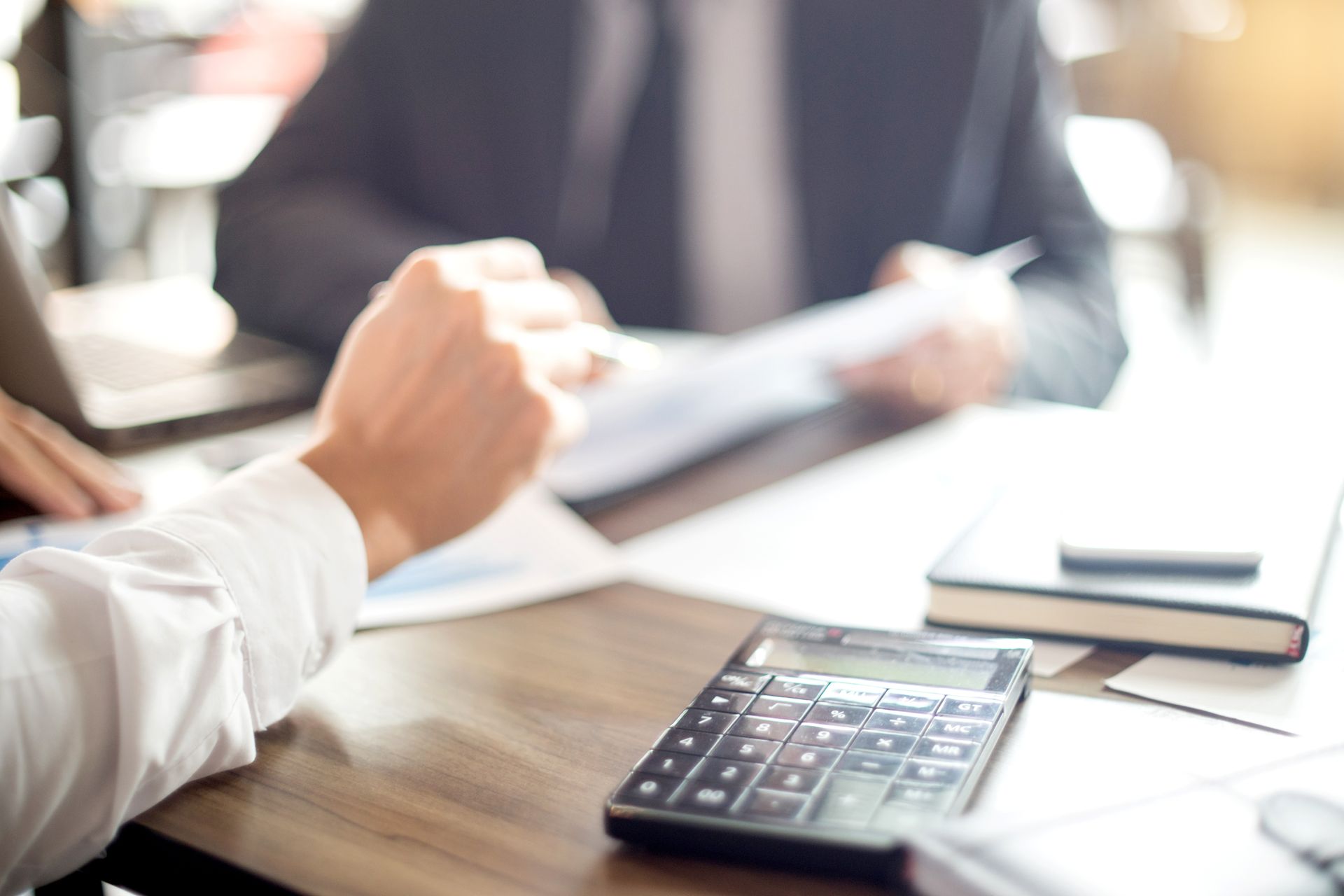 Calculator and documents on a meeting table with people discussing in the background Calculator and documents on a meeting table with people discussing in the background