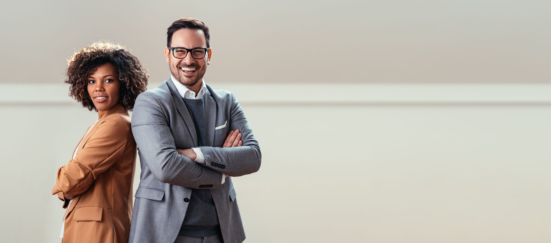 Two professionals standing back-to-back in a bright office, arms crossed and smiling Two professionals standing back-to-back in a bright office, arms crossed and smiling