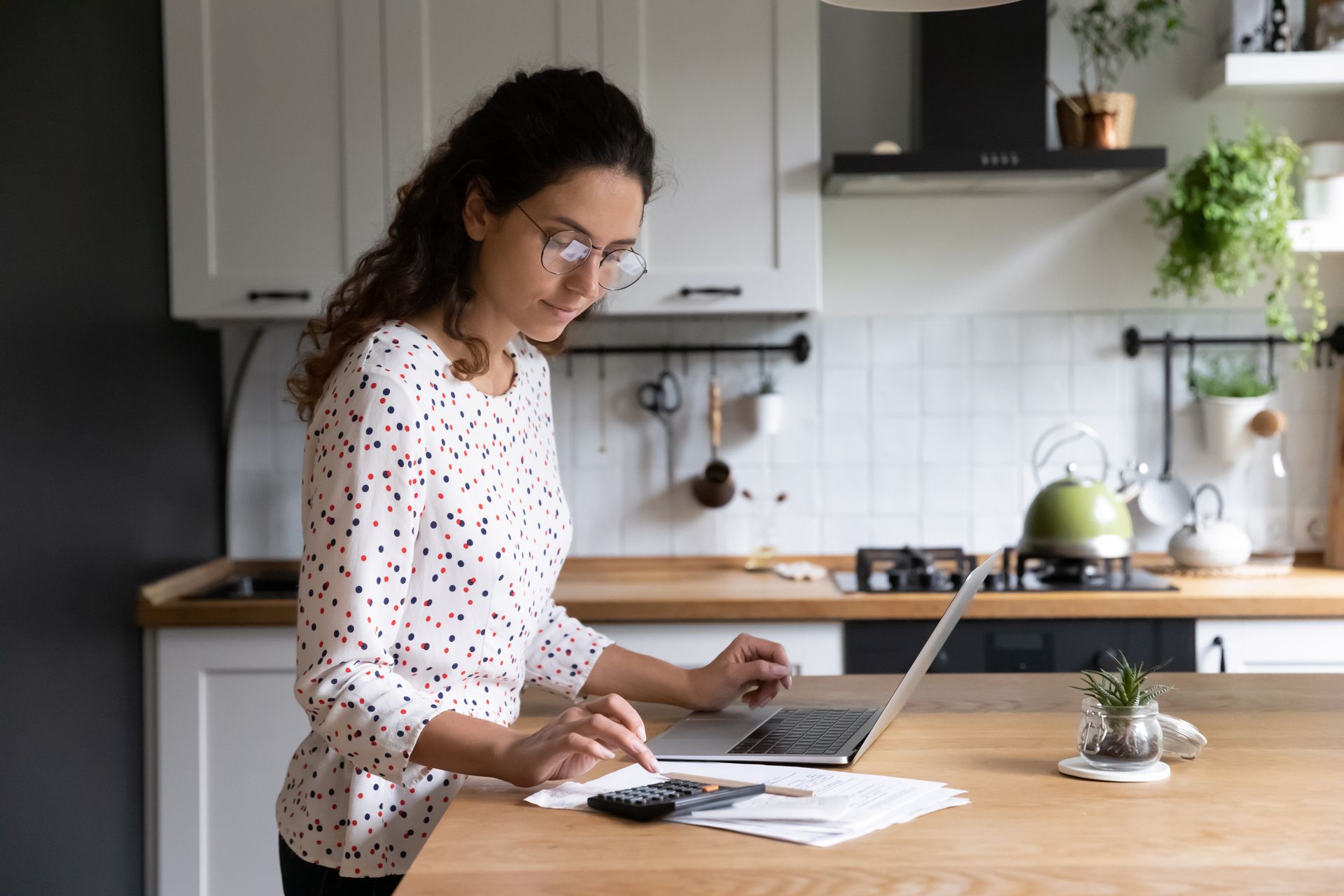 Person standing at a kitchen counter using a laptop and writing on papers. Person standing at a kitchen counter using a laptop and writing on papers.