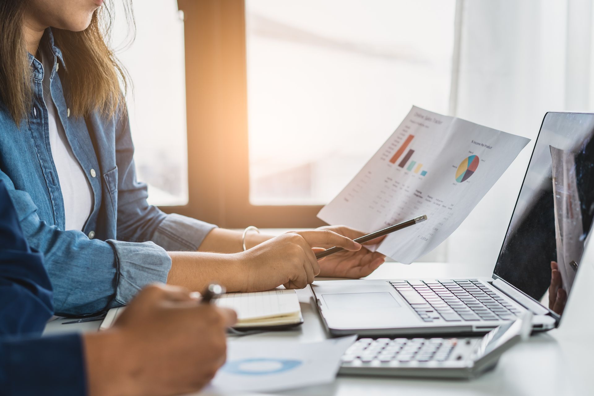 Two coworkers reviewing financial charts at a desk with a laptop and notebook Two coworkers reviewing financial charts at a desk with a laptop and notebook