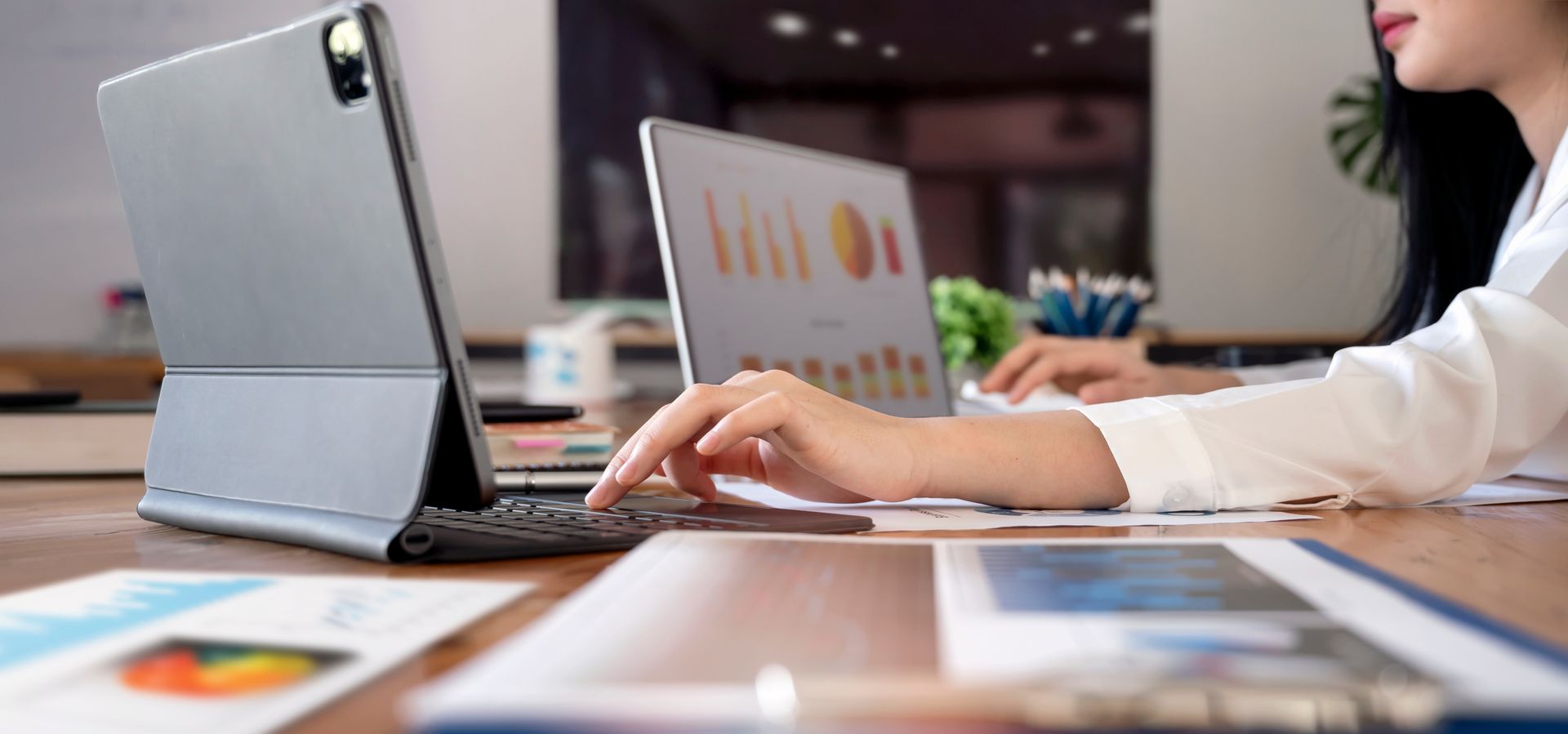 Person typing on a laptop beside a tablet showing charts in a modern office Person typing on a laptop beside a tablet showing charts in a modern office