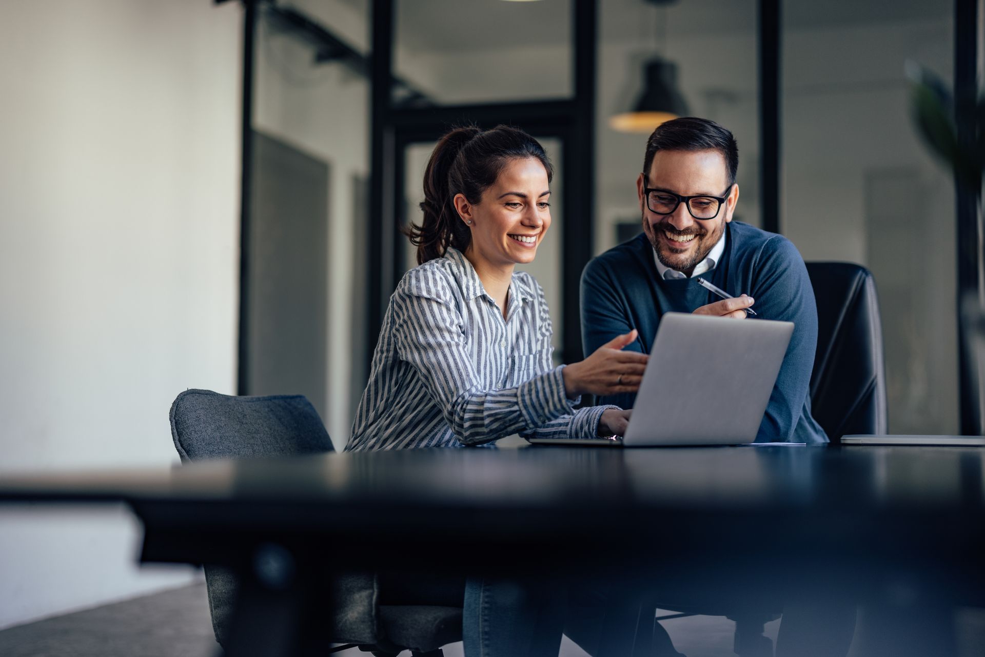 Two coworkers smiling at a laptop in a modern office meeting room Two coworkers smiling at a laptop in a modern office meeting room